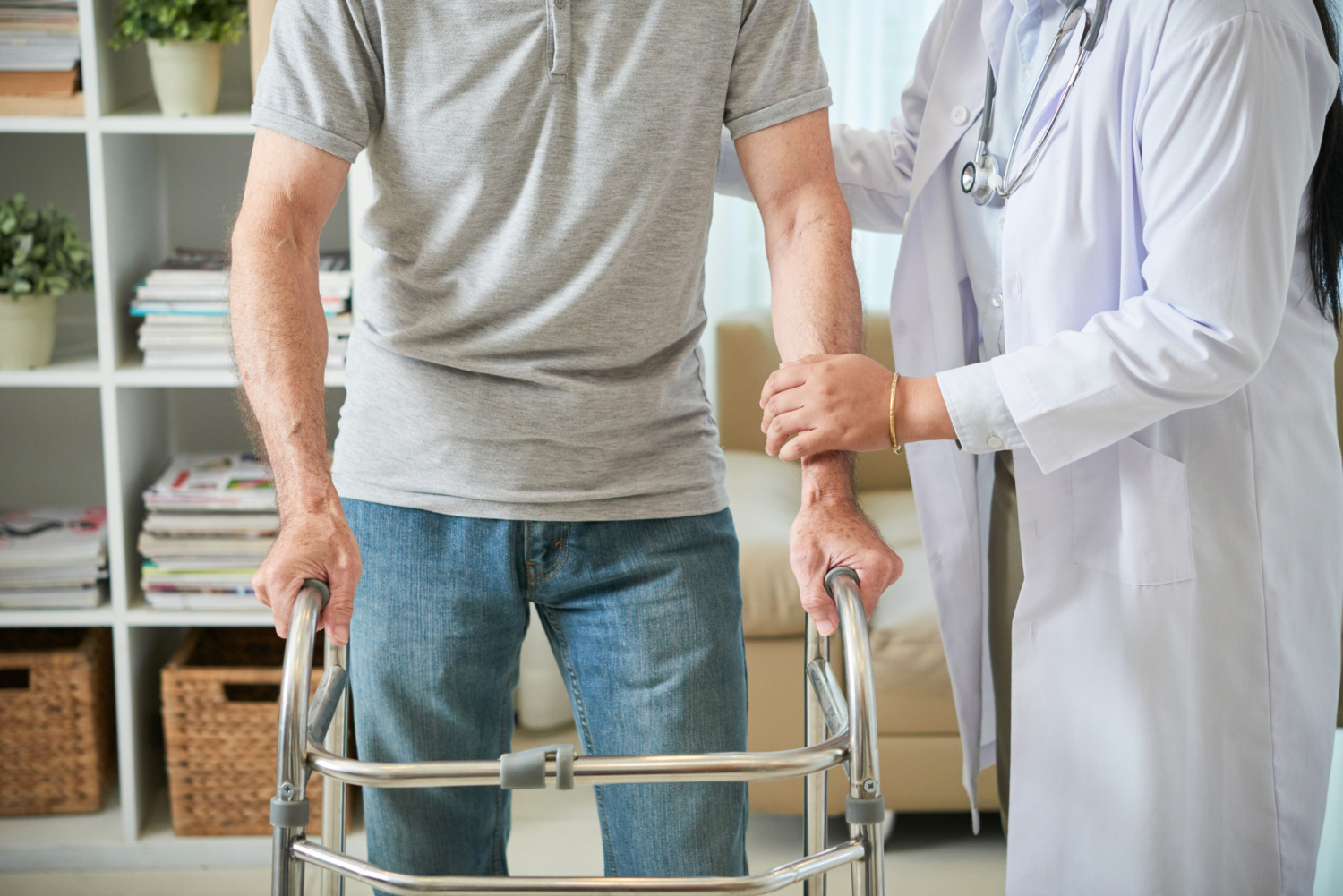 unrecognizable-female-doctor-helping-male-patient-walk-with-walking-frame